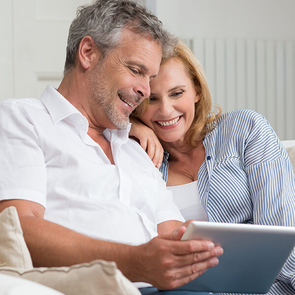 Couple on the couch A Couple in their 50s enjoying their time while sitting on the couch browsing a tablet.