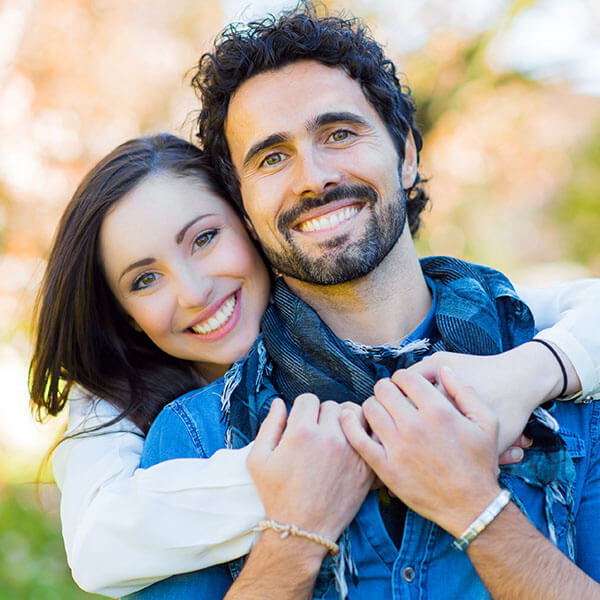 A young couple in a park smiling as they hug
