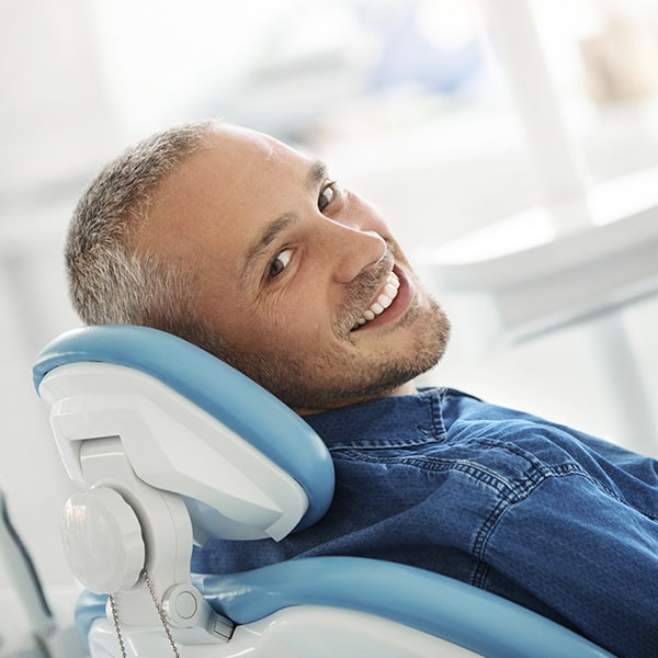 How do porcelain veneers work? A man lying in a dental chair while showing his white teeth