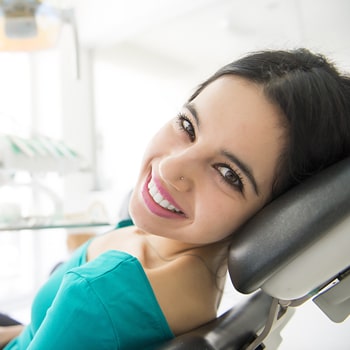 Lady smile a lady with a black hair sitting on a dental chair looking at her left showing her beautiful smile