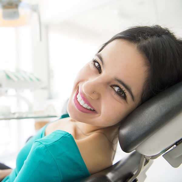 Lady smile a lady with a black hair sitting on a dental chair looking at her left showing her beautiful smile