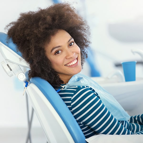 Learn how we extract teeth A young woman smiling and sitting in a dental chair while wearing a dental bib