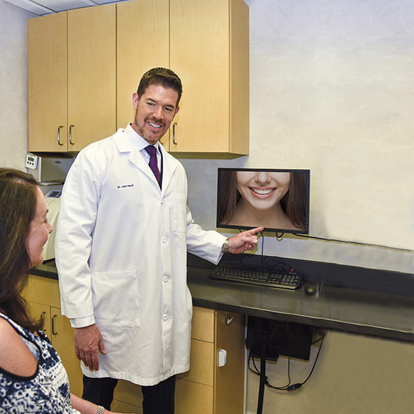 Two male dentists presenting a picture of a bright white smile to a lady patient who is sitting in front of them