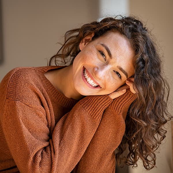A lady with long curly hair with her head tilted on her left arms