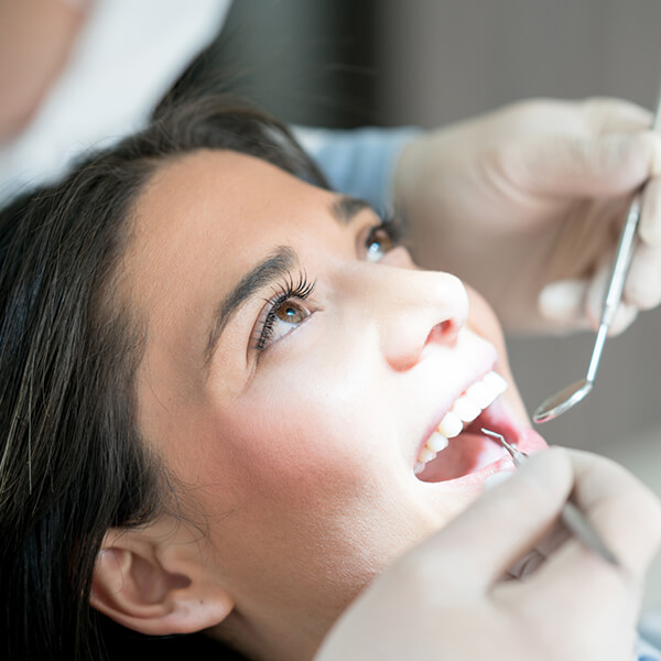 Woman Having a Dental Check-up A woman is lying on a dental chair and opens her mouth while the dentist examines her teeth