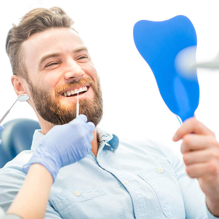 Man holding hand mirror A man sitting on a dental chair looks at a hand mirror while receiving a dental procedure