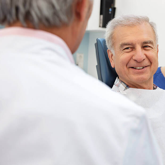 Man discussing with a Team Member A man is sitting on a dental chair is looking and talking to the Team Member