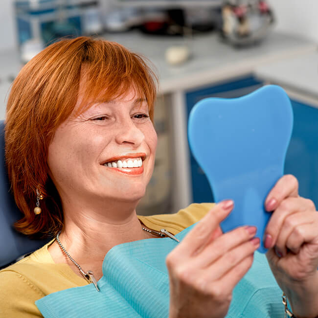 Woman examines her smile A woman lying on a dental chair is while looking at her smile in the mirror she is holding