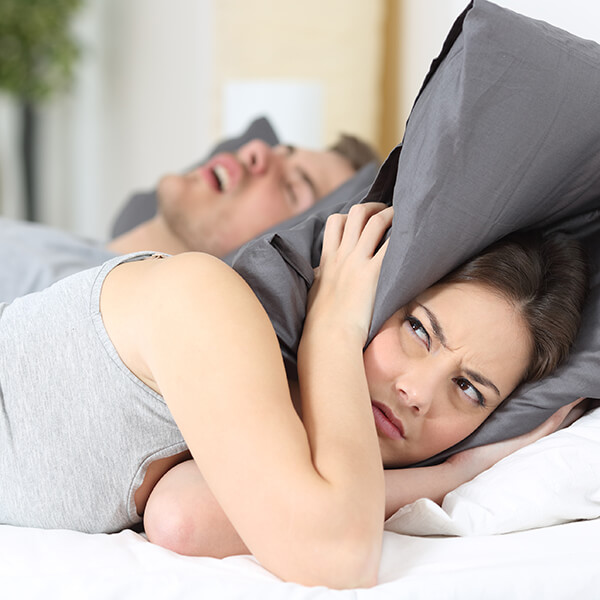 Sleep-Apnea a wife covers her ears with a pillow while husband is asleep