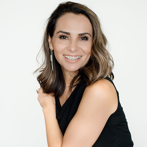 A smiling woman wearing sleeveless blouse posing on her left side while her left arms holds her right shoulder